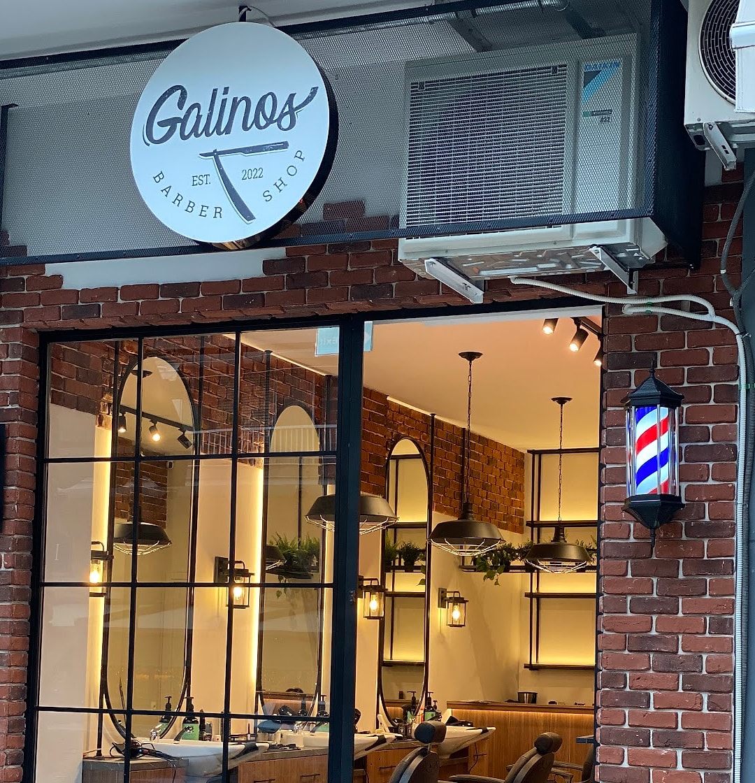 Η βιτρίνα του Galinos Barbershop με το στρογγυλό σήμα, το τούβλο και τη μπαρμπερόμπαρα